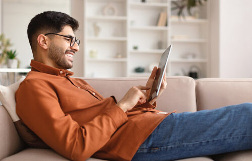 Smiling young Arab man using digital tablet at home