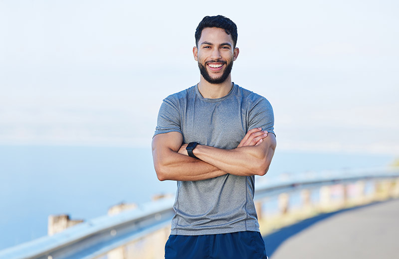 Man athlete, healthy and with cross arms, smile and stand happy outdoor for workout, warm up and wellness..Portrait, confident male and trainer ready for training, fitness and enjoy health exercise